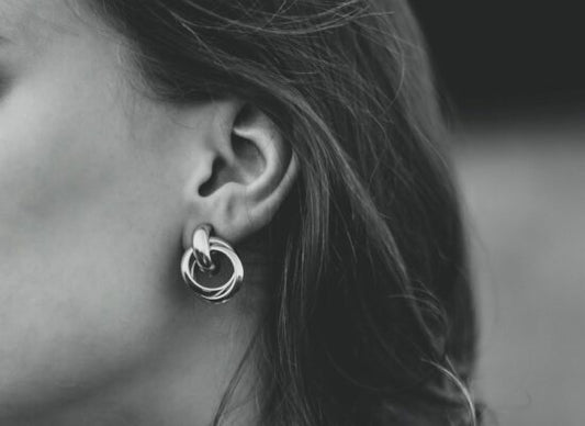 A black-and-white close-up of a person's ear wearing a large, twisted hoop earring, with dark hair partially visible against a blurred background.