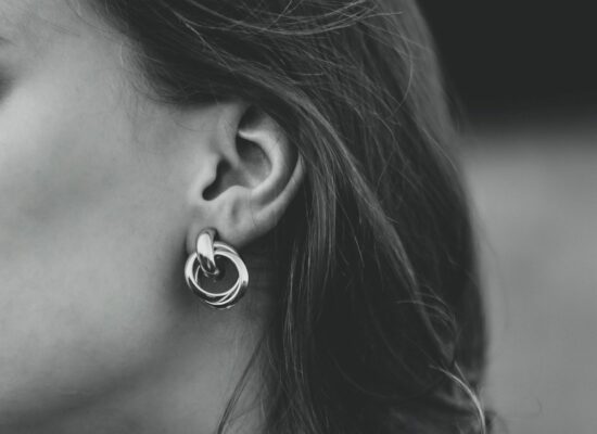 A black-and-white close-up of a person's ear wearing a large, twisted hoop earring, with dark hair partially visible against a blurred background.
